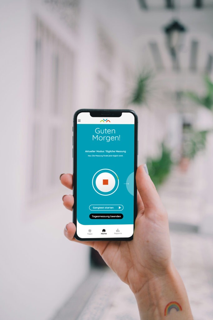 Eine weibliche Person hält ein Smartphone in die Luft auf dem der Start-Screen zur Tagesmessung und Gangtests der ParkinsonGo App zu sehen ist.