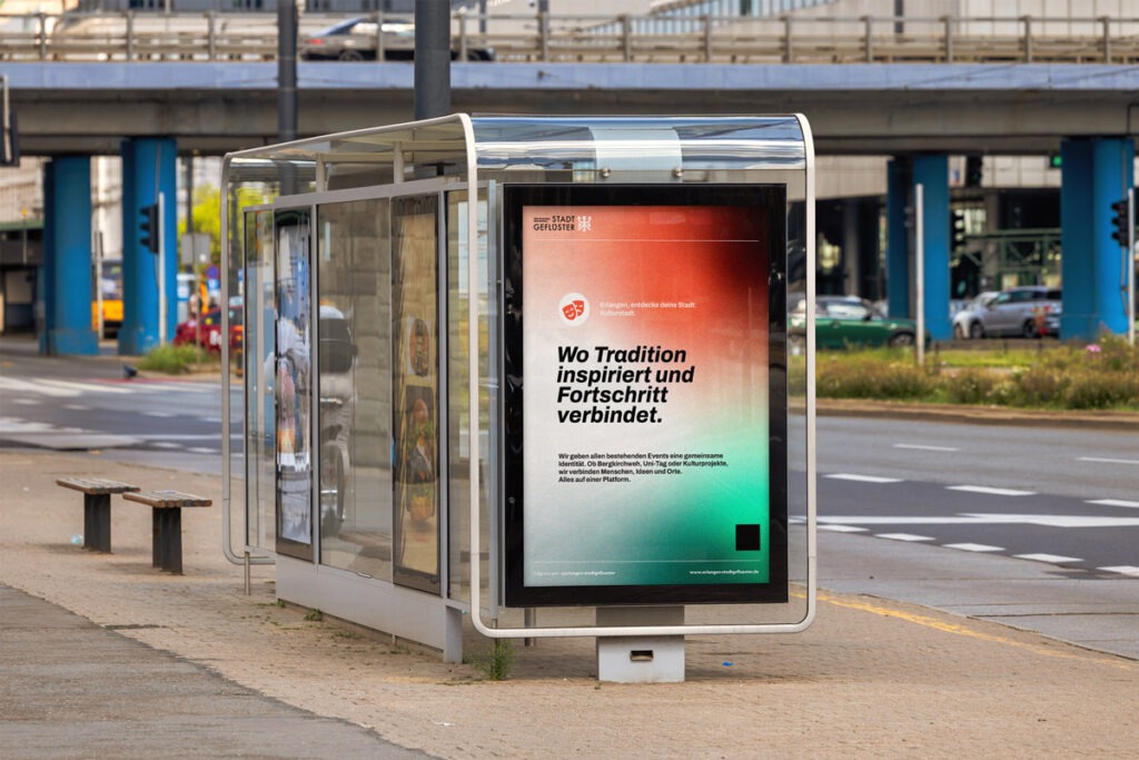 Eine Bushaltestelle zeigt eine plakatierte Wand mit dem Design von der Stadtinitiative "Stadtgeflüster". Im Hintergrund ist eine Brücke mit Straßenunterführung.